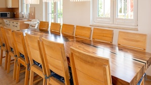 Un espace de salle à manger moderne, avec une table et des chaises en bois, des luminaires suspendus et de grandes fenêtres.
