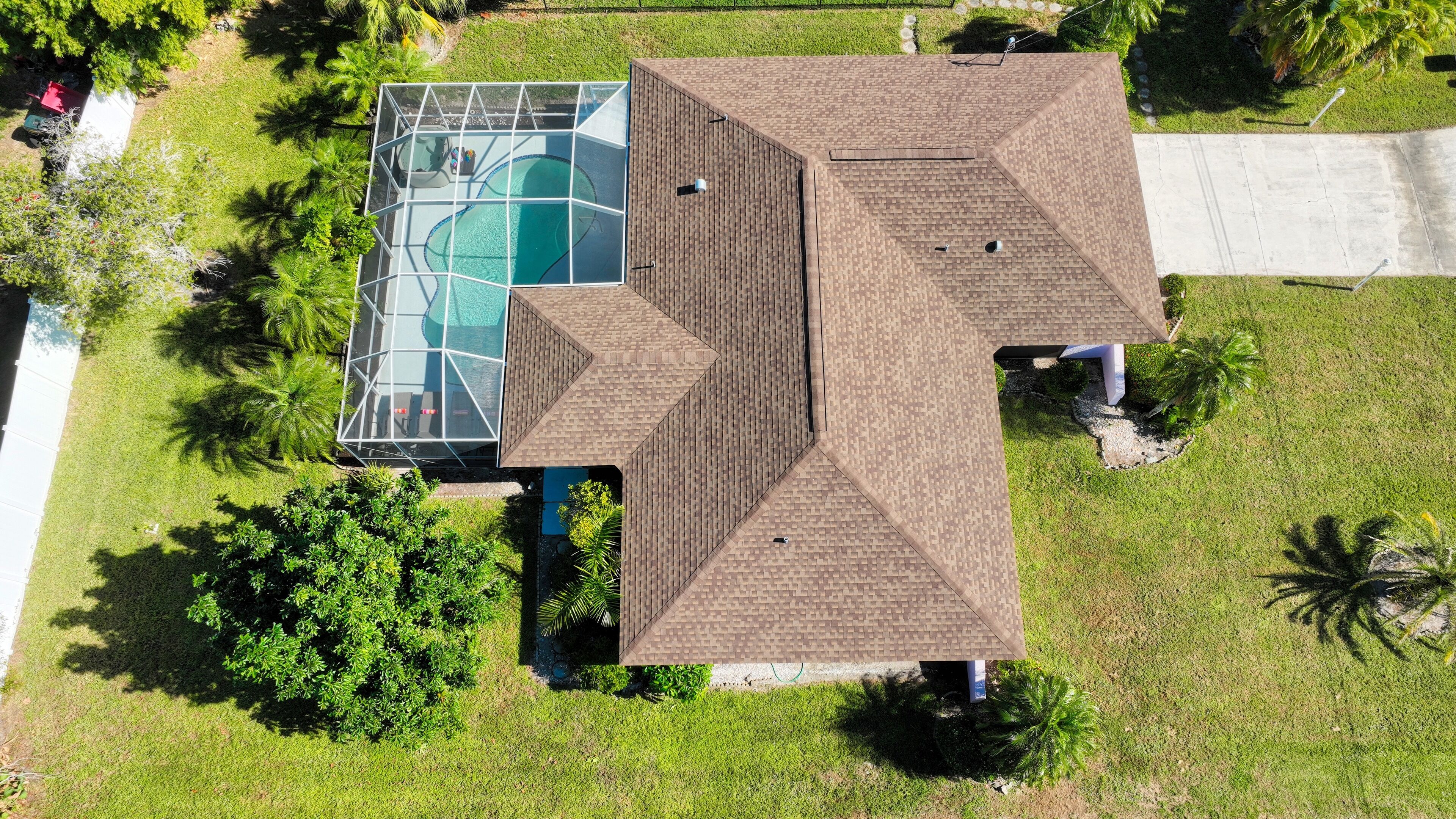 An aerial view of a house with a swimming pool, surrounded by lush greenery and palm trees.