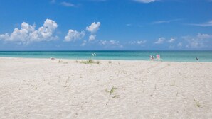 Een strand met heldere lucht, enkele personen en een paar stoelen in het zand.