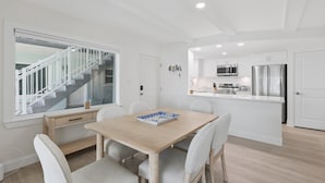 Een moderne keuken met roestvrijstalen apparatuur, een eethoek met een houten tafel en stoelen, en een trap die naar een verdieping leidt.