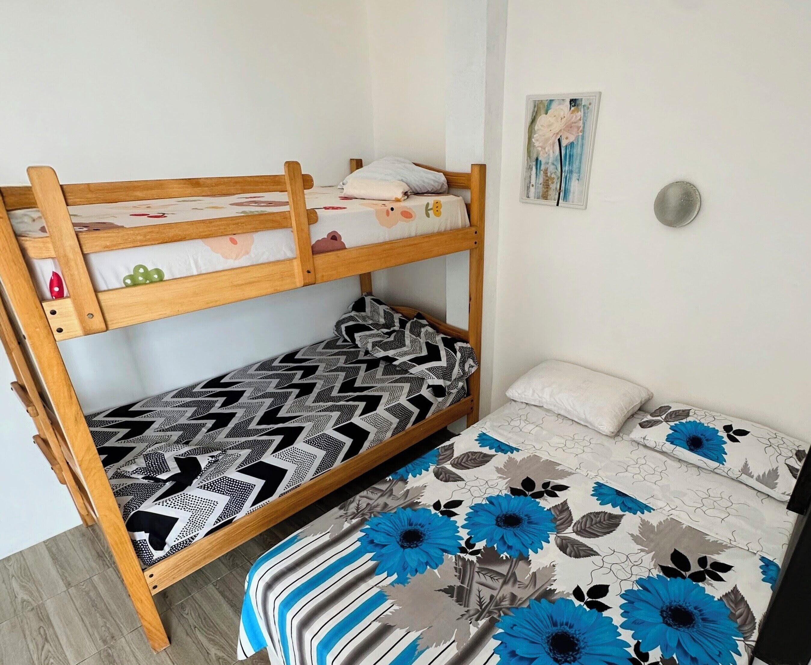 A bunk bed with patterned bedding, a wall-mounted light, and a floral painting.