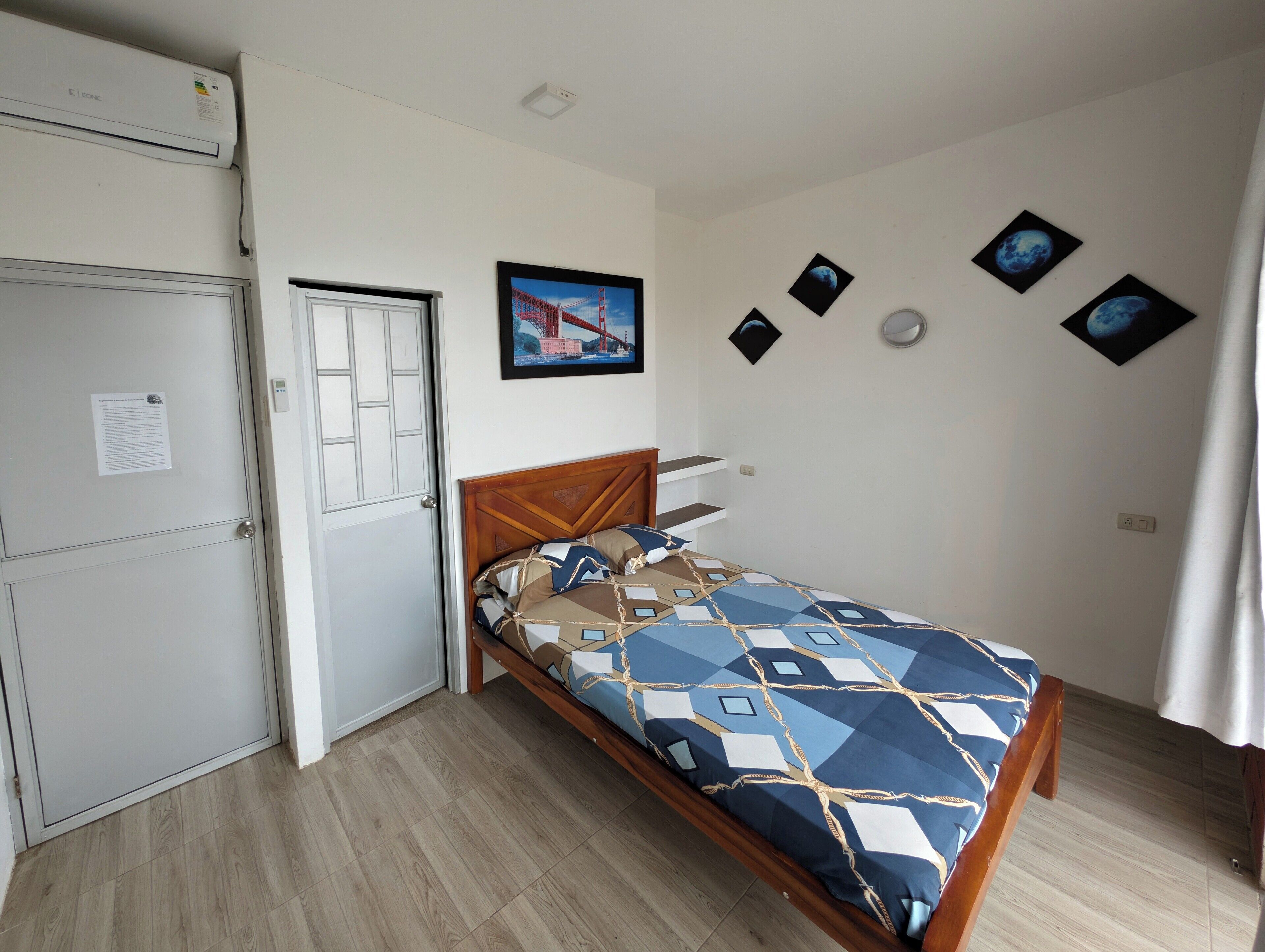 A bedroom with a bed, a wardrobe, a door, and a wall with pictures.