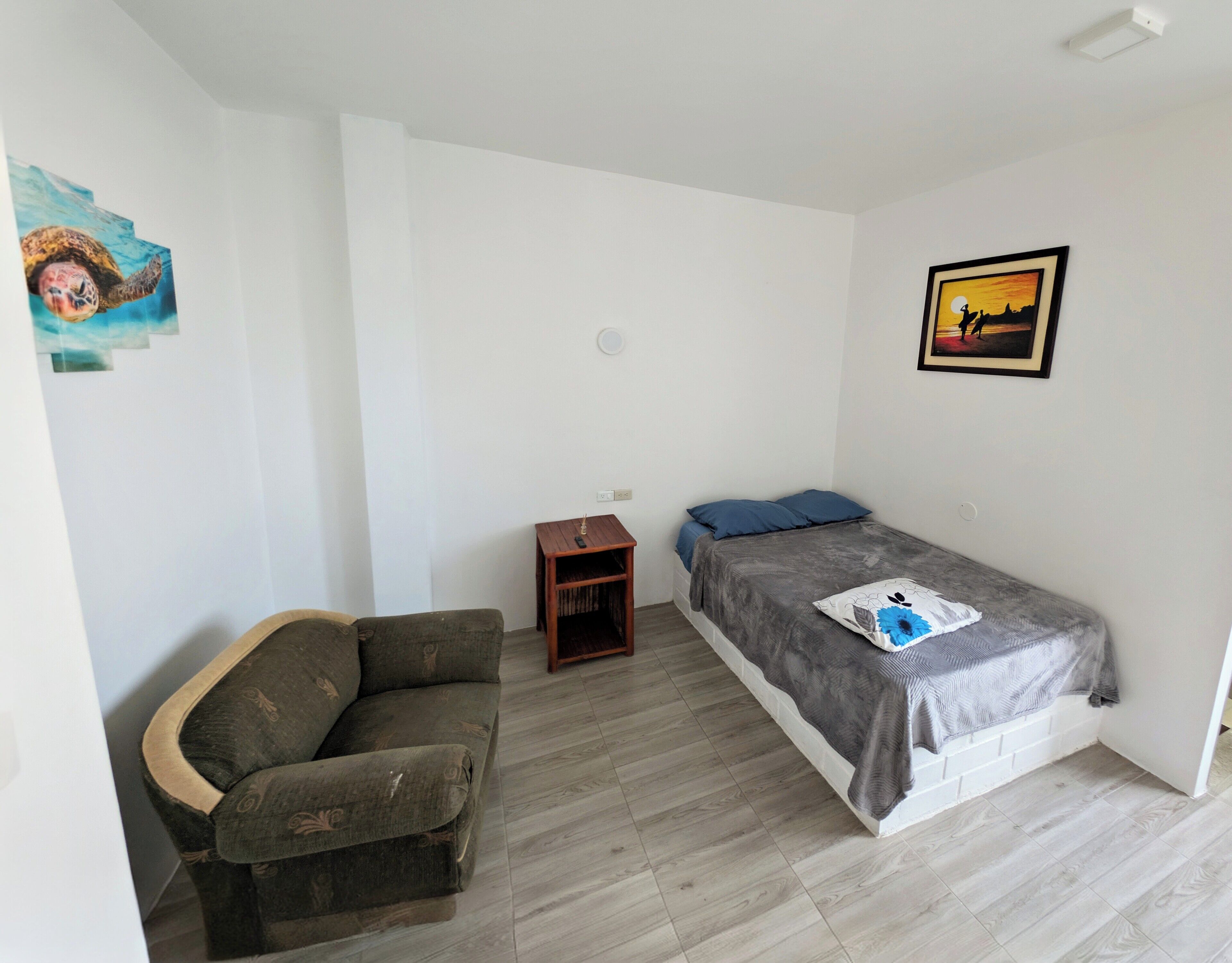 Una habitación pequeña y poco amueblada, con una cama, una mesita y un sofá.