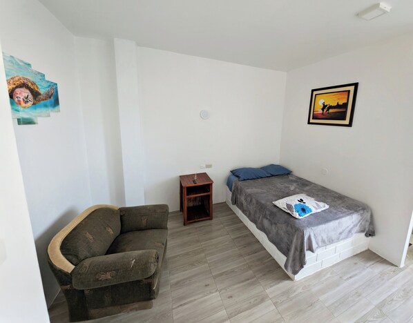 Una habitación pequeña y poco amueblada, con una cama, una mesita y un sofá.