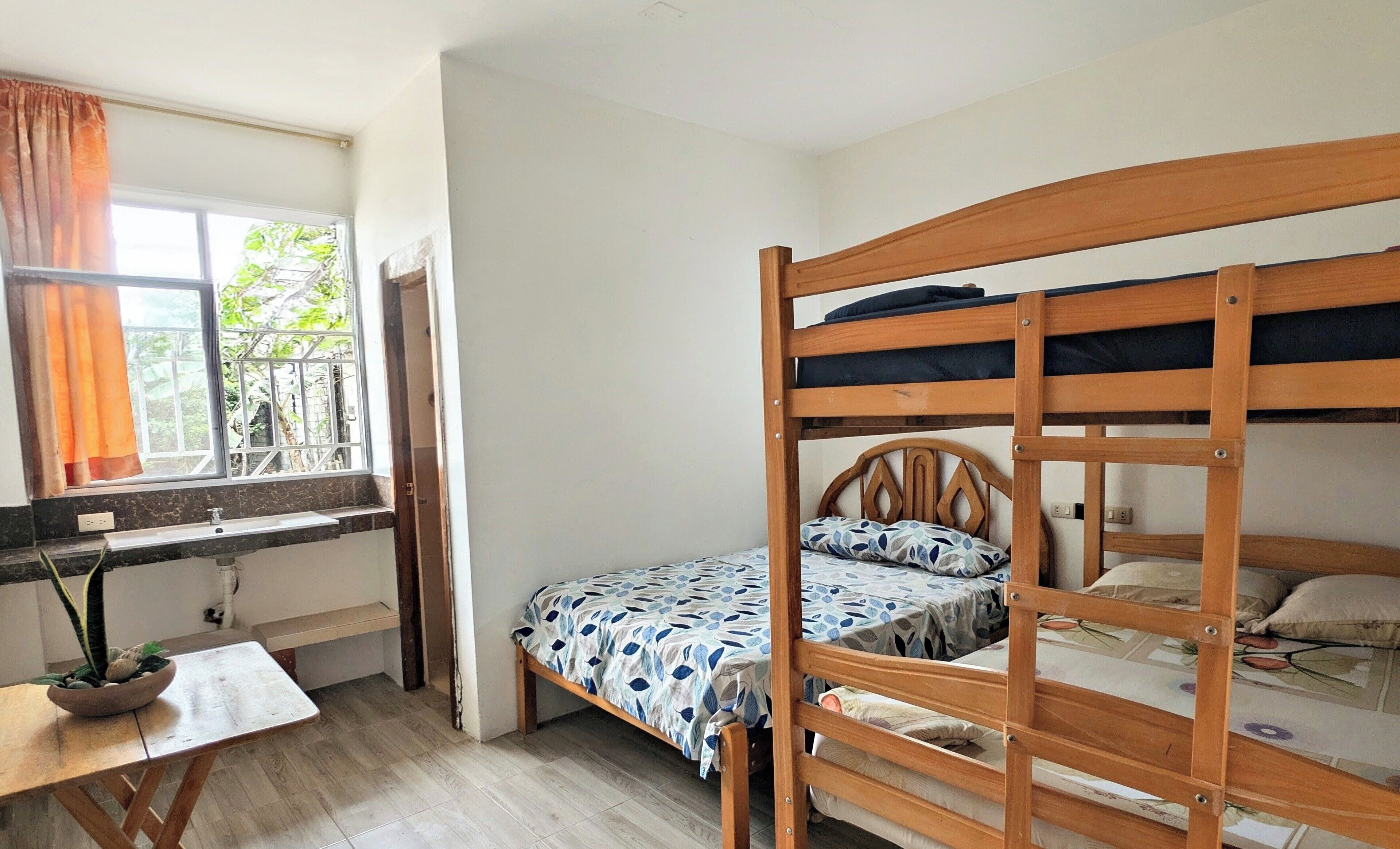 A dormitory room with bunk beds, a desk, and a window with curtains.
