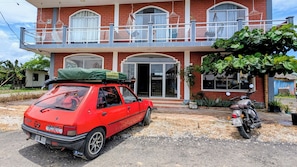 Un coche rojo estacionado frente a un edificio de dos pisos con balcón.