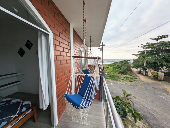 Un balcón con una hamaca, una cama y vista al océano.