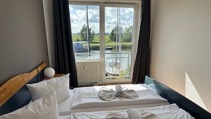 Hotellihuone, jossa on kaksi sänkyä ja ikkunasta avautuu näkymä veneeseen ja vehreään maisemaan.