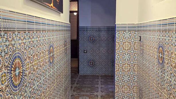 Un couloir orné de motifs complexes en mosaïque, un ventilateur de plafond et une œuvre d’art encadrée accrochée au mur.