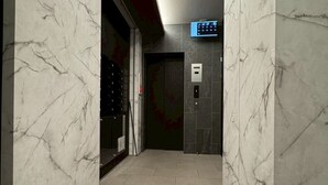 Un pasillo con paredes de mármol y piso de baldosas, que conduce a un ascensor con teclado y puerta.