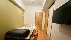 Um quarto com uma cama, uma televisão presa na parede e um guarda-roupa.