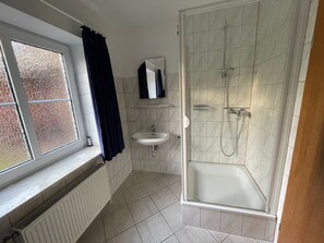 Ett badrum med ett fönster, ett handfat, en spegel och en dusch.