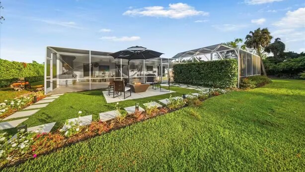 Ein modernes Haus mit einer gläsernen Veranda, einem Esstisch und Sitzgelegenheiten im Freien.