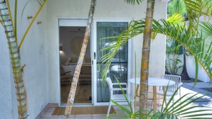 Eine Terrassenfläche mit einer Schiebetür zu einem Raum, einem weißen Tisch und Stühlen sowie mehreren Palmen.