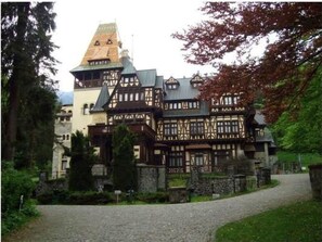 A traditional half-timbered building with a prominent tower, surrounded by lush greenery and a gravel path.