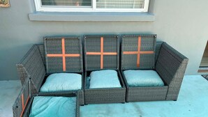 Un canapé en osier agrémenté de touches orange et de coussins turquoise, placé sur une terrasse en béton.