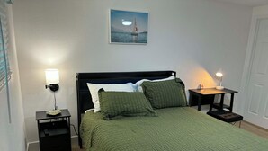 Un lit bien fait, recouvert d’une couette verte, deux tables de chevet avec des lampes, un tableau encadré au mur et un plancher en bois.