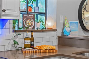 Eine Küchenarbeitsplatte mit einer Olivenölflasche, einem Schneidebrett mit Brot, einem Salzstreuer und einer dekorativen Gartenzwerg.