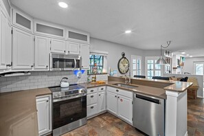 A modern kitchen with white cabinetry, stainless steel appliances, and a central island with a sink. - Ocean Peek • hot tub • king bed - 3br/2.5ba (Cape Canaveral)