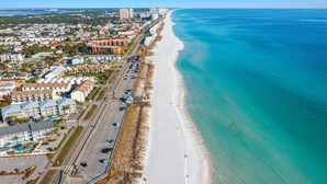An aerial view of a coastal city with a long sandy beach, a dense urban area with multi-story buildings, and a clear blue sea. - NEW: Destin's Premier Wedding & Corporate Retreat | Outdoor Pavilion | Resort Pool (Miramar Beach)