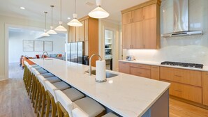 A modern kitchen with a long island, wooden cabinets, stainless steel appliances, and pendant lighting. - NEW: Destin's Premier Wedding & Corporate Retreat | Outdoor Pavilion | Resort Pool (Miramar Beach)