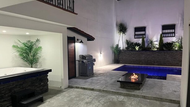Ein moderner Poolbereich im Innenbereich mit einer Steinsitzbank, einem Grill und einem kleinen Feuerbereich.