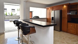 Eine moderne Küche mit einer zentralen Kochinsel, Barhocker, Holzschränken und einem Edelstahlkühlschrank.