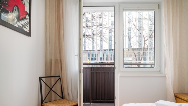 A bedroom with a bed, a chair, a window, and a door leading to an outdoor area. - Twarda Downtown Apartment (Warszawa)