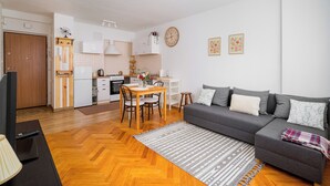 A modern living room with a grey sofa, wooden floor, and a kitchen area in the background. - Twarda Downtown Apartment (Warszawa)