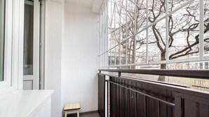 A balcony with a view of bare trees, a small wooden stool, and a metal railing. - Twarda Downtown Apartment (Warszawa)