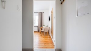 A narrow hallway with wooden flooring leading to a room with a table, chair, and a TV mounted on the wall. - Saska Kępa Lavish Studio (Warszawa)