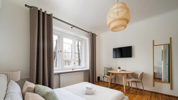 A bedroom with a bed, a desk, a chair, a television, and a window with curtains. - Saska Kępa Lavish Studio (Warszawa)