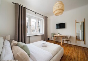 A bedroom with a bed, a desk, a chair, a television, and a window with curtains. - Saska Kępa Lavish Studio (Warszawa)