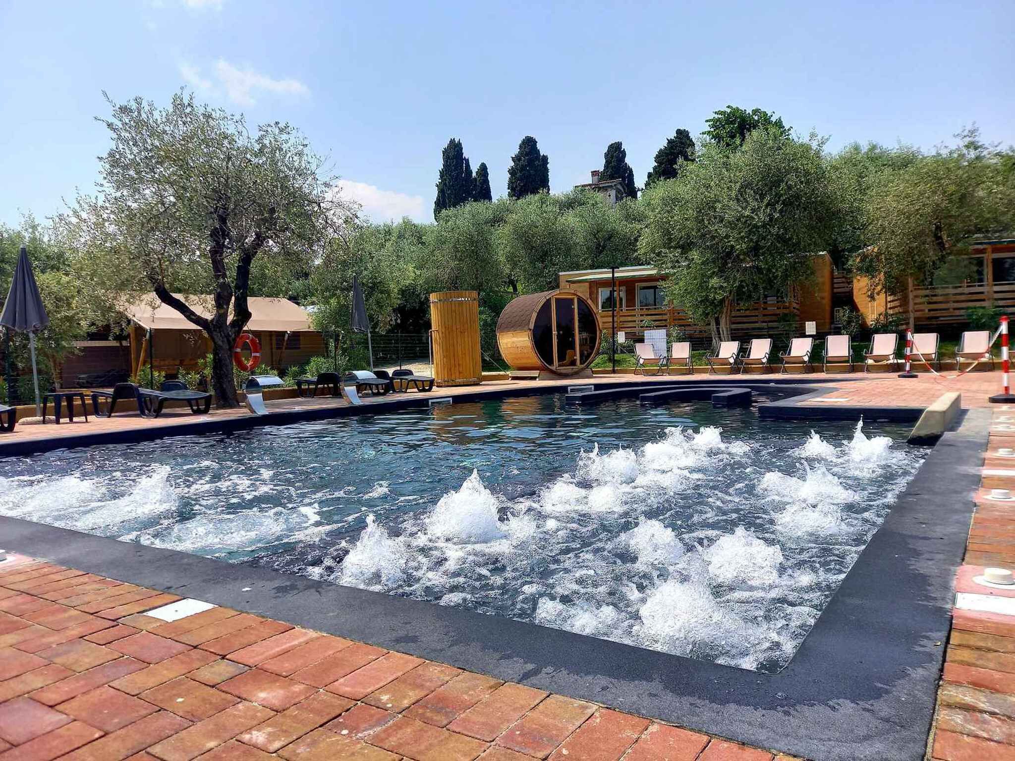 A swimming pool with water jets, lounge chairs, and a wooden barrel structure.