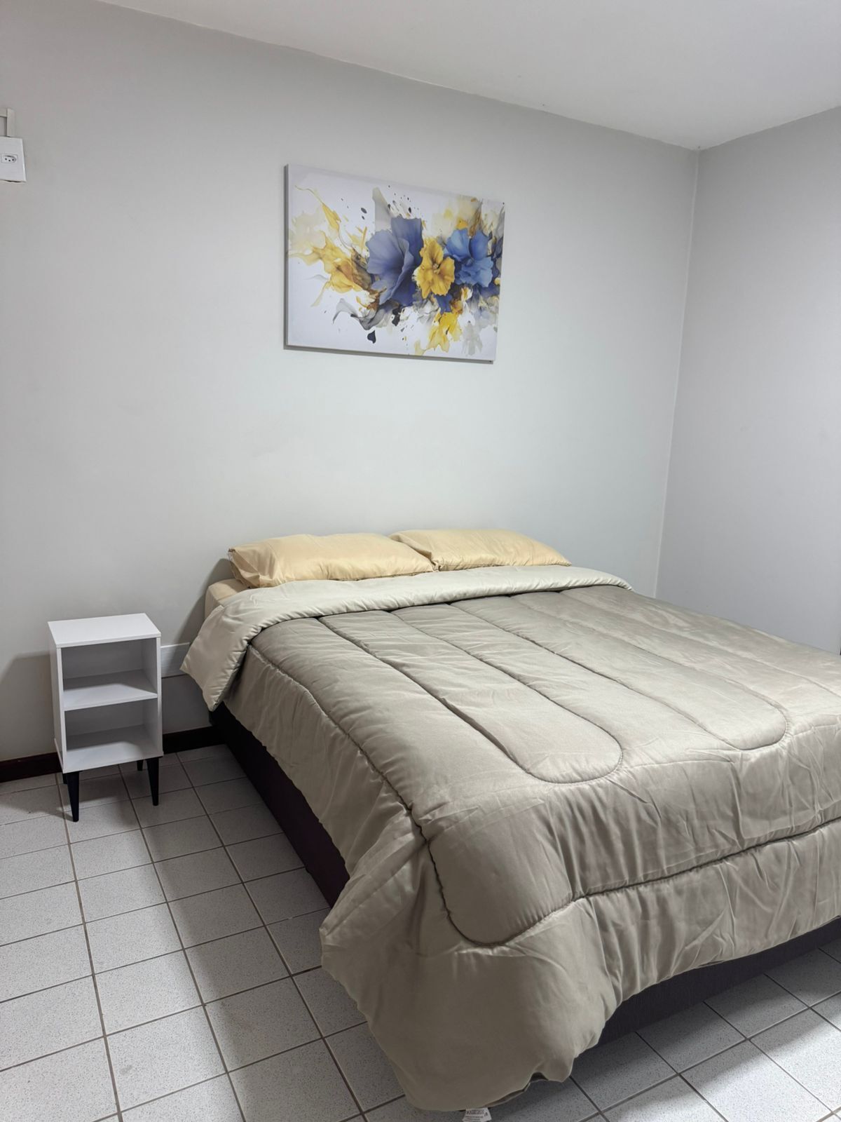 Ein Schlafzimmer mit einem Bett, einem Nachttisch und einem an der Wand hängenden abstrakten Gemälde.