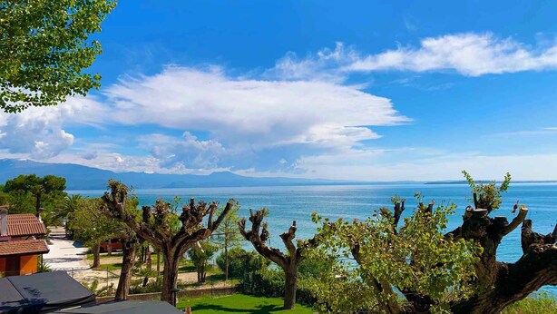 A coastal landscape with a clear view of the sea, a tree-lined path, and distant mountains. - Mobile home with air conditioning, terrace and pool (Padenghe sul Garda)