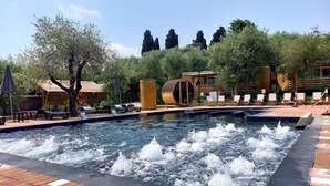 A swimming pool with water jets, lounge chairs, and a wooden barrel structure. - Mobile home with air conditioning, terrace and pool (Padenghe sul Garda)