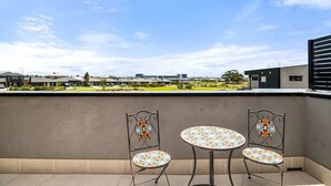 Un balcón con dos sillas y una mesa, con vista a una zona residencial con casas y un parque.