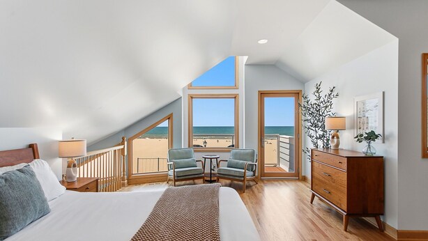 Un dormitorio con una cama grande, un escritorio, dos sillas, un aparador y un balcón con vistas a la playa.