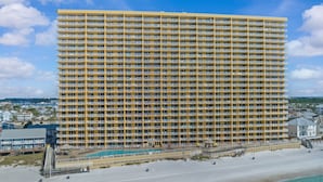 Et højt hotel med flere balkoner, en pool og udsigt til stranden.