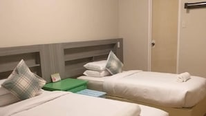 Habitación de hotel con dos camas, cada una con ropa blanca y una almohada. Hay una mesita de noche verde y una puerta en la habitación.