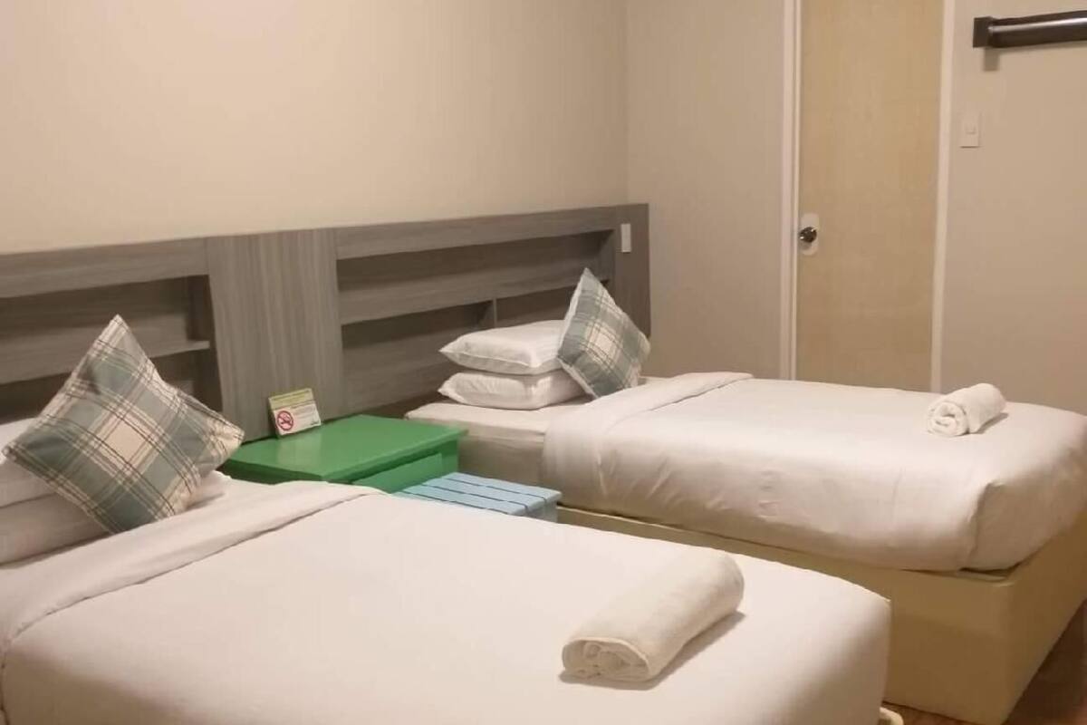 Une chambre d’hôtel avec deux lits, chacun étant équipé de draps blancs et d’un oreiller. On y trouve une table de chevet verte et une porte.