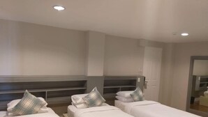 Habitación de hotel con tres camas individuales, cada una con una almohada y una toalla enrollada.