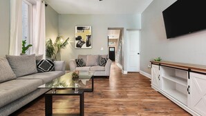 Una sala de estar moderna con un juego de sofá, una mesa de centro de vidrio y un televisor montado en la pared.