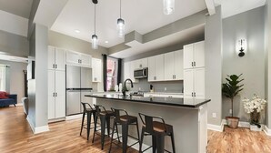 Una cocina moderna con armarios blancos, una isla central con taburetes y luminarias colgantes.