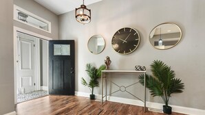 Un pasillo con una puerta negra, una consola decorada con objetos y tres relojes de pared.