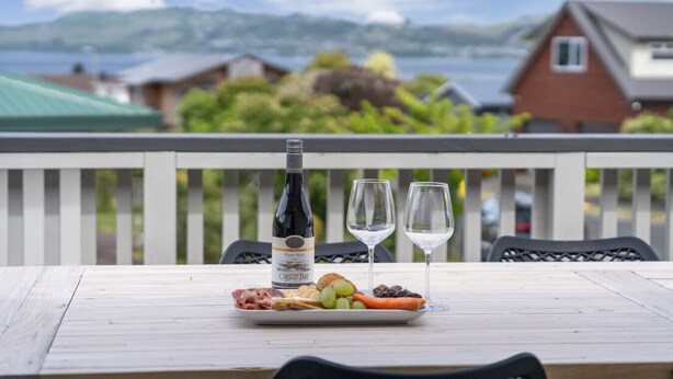 Une table avec une bouteille de vin, deux verres et une assiette de nourriture, le tout placé sur un balcon donnant sur un paysage magnifique.