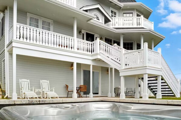 A two-story house with a covered porch, a hot tub, and outdoor seating.