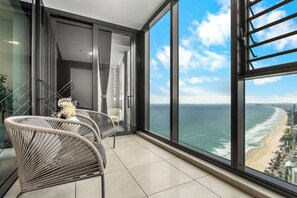 Ein Balkon mit Korbstühlen, einem kleinen Tisch mit einer Vase und Blick auf das Meer und den Strand.