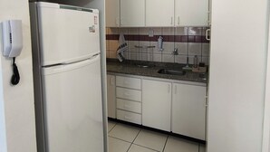 Cocina compacta con gabinetes blancos, refrigerador empotrado, lavamanos y teléfono.